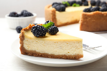 Piece of delicious cheesecake decorated with blackberries on table
