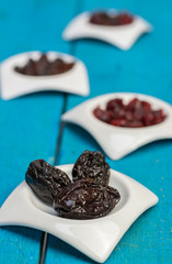 Food,taste and snack concept: dried plums in small white saucers on a wooden blue background.