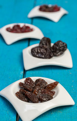 Dried raisins in small white saucers on a wooden blue background.