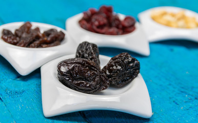 Food,taste and snack concept: dried plums in small white saucers on a wooden blue background.