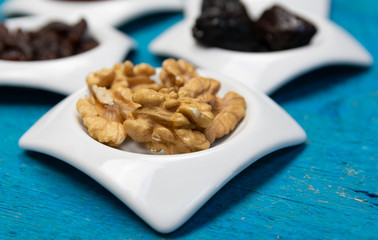 Food,taste and snack concept: walnuts in small white saucers on a wooden blue background.