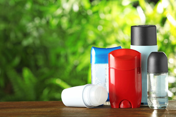 Set of different deodorants on wooden table against blurred green background. Space for text