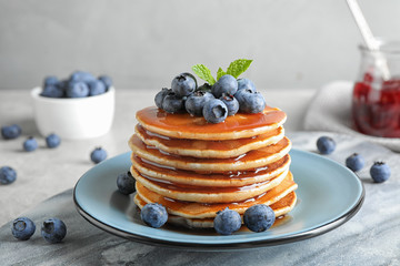 Plate of delicious pancakes with fresh blueberries and syrup on grey table against light background - obrazy, fototapety, plakaty