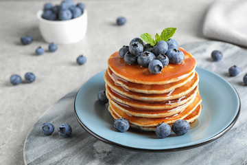 Plate of delicious pancakes with fresh blueberries and syrup on grey table