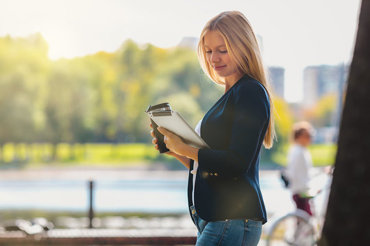 Young Happy Smiling Caucasian Adult Girl Business Student Walking Concept In The Park Holding Reading Tablet Thinking Of Credit Finance Job In The College With Wireless Headphones Drink Coffee