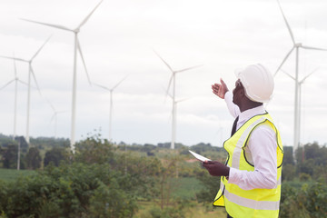 African Engineer standing and hoding laptop with wind turbine