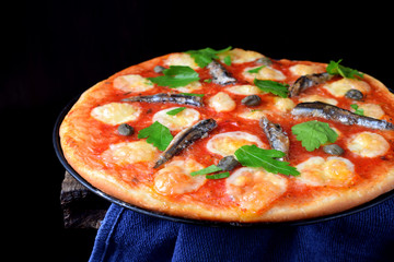 Round pizza with anchovies, capers, mozzarella and tomato sauce garnished with fresh parsley