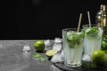 Glasses of delicious Mojito cocktail with ice and mint on grey table against black background. Space for text