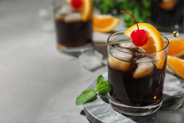 Glass of delicious cocktail decorated with cherry and orange on light grey table, closeup. Space for text