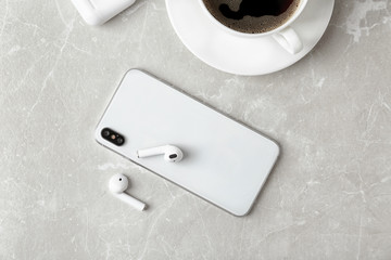 Flat lay composition with wireless earphones and mobile phone on light grey marble table