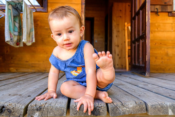 Fototapeta premium Baby sitting on the porch of his wooden house on vacation.