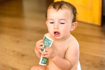 Baby sniffing money, a dollar bill, with weird and funny expression.