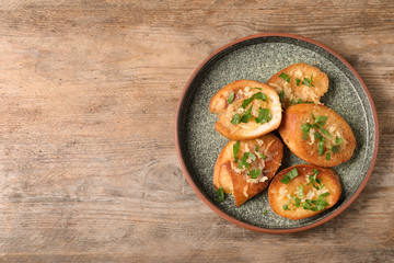 Slices of toasted bread with garlic, cheese and herbs on wooden table, top view. Space for text