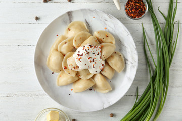 Delicious cooked dumplings with sour cream on white wooden table, flat lay