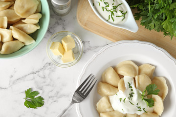 Delicious cooked dumplings with sour cream on white marble table, flat lay