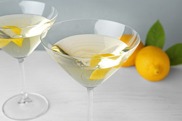 Glasses of lemon drop martini cocktail with zest on white wooden table against grey background