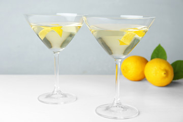 Glasses of lemon drop martini cocktail with zest on white wooden table against grey background