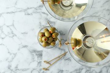 Flat lay composition with glasses of Classic Dry Martini and olives on white marble table. Space for text