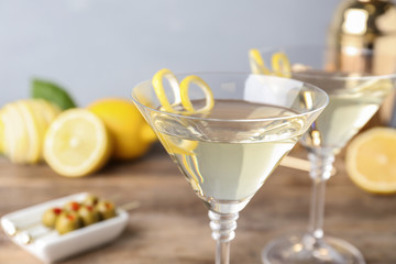Glasses of lemon drop martini cocktail with zest on wooden table against grey background