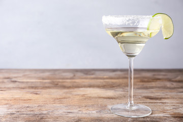 Glass of lemon drop martini cocktail with lime slice on wooden table against light background. Space for text