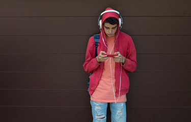 young boy or student with mobile phone and headphones on the background wall outdoors
