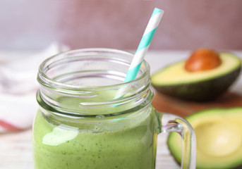 Mason jar of tasty avocado smoothie with straw on table, closeup