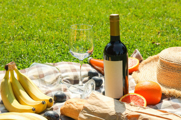 Bottle of wine, baguette, fruits, straw hat and towel on grass, space for text