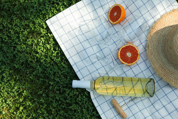 Bottle of wine, glasses, orange, corkscrew, towel and straw hat on grass, space for text