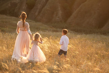 A young mother with children walks in a field at sunset. Country style