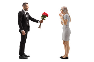 Young man smiling and giving a bunch of red roses to a surprised woman