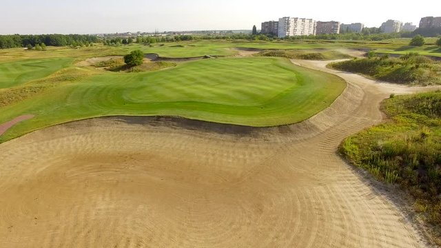 4K aerial footage of golf course. Cinematic top view shot with green grass, ponds, watercourses, palm trees, patches, holes, flags. Drone flies along the field during sunset. Vacation video concept