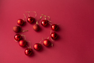 Red Christmas tree decorative toy balls on red celebratory Christmas background laid out in the shape of a heart. New Year's holidays. Christmas holidays