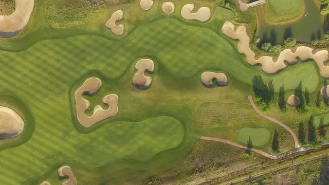 4K aerial footage of golf course. Cinematic top view shot with green grass, ponds, watercourses, palm trees, patches, holes, flags. Drone flies along the field during sunset. Vacation video concept