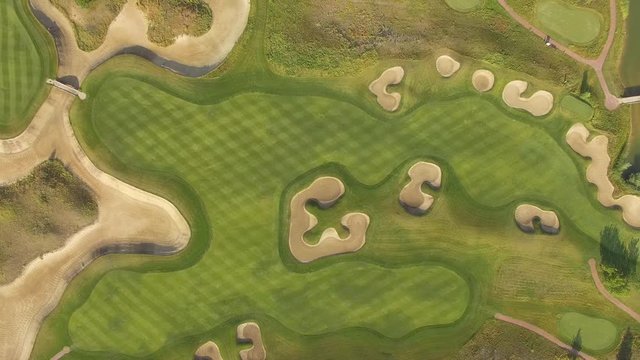 4K aerial footage of golf course. Cinematic top view shot with green grass, ponds, watercourses, palm trees, patches, holes, flags. Drone flies along the field during sunset. Vacation video concept