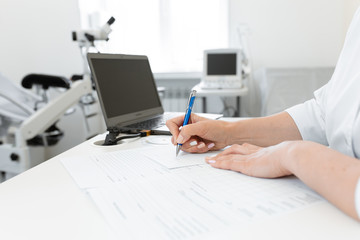 gynecologist doctor writes a recipe on a sheet of paper, on the background of a gynecological chair