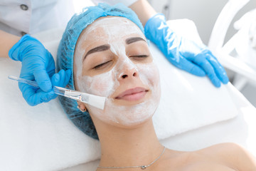 A professional cosmetologist applies a nourishing cream on the patient's face. Moisturizing, cleaning and facial skin care.