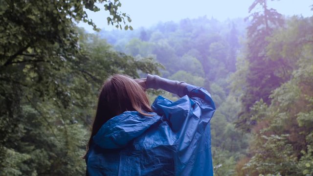 Girl in a blue raincoat photographs the mountains in the forest.