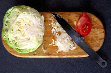 Chopped cabbage and piece of tomato on a cutting board with a knife, top view