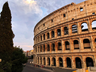 Fototapeta na wymiar colosseum in rome across square, tourists, trees, buildings and sunset skyline 