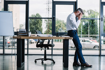 businessman touching head while standing near table in modern office