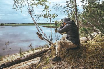 A man with a pick-up in a gray jacket, photographs nature on the banks of the river, in the forest