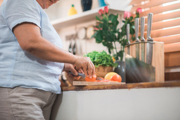 Asian elderly couple cut tomatoes prepare ingredient for making food in the kitchen, Couple use organic vegetable for healthy food at home. Lifestyle senior family making food at home concept.