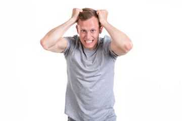 Headache. Young man in a gray t-shirt is screaming and holding his head, isolated on a white background.