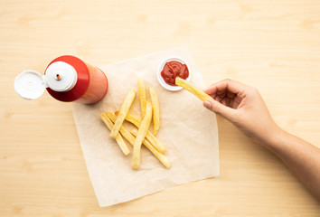 Top view of youngwoman dipping french fried  with tomato sauce ( ketchup ) on wood table background.