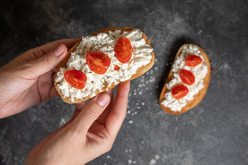 Bruschetta with tomatoes and cheese in the hands on a dark background, top view.