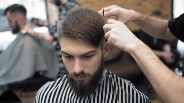 Close up on Men's hairstyling and haircutting in a barber shop or hair salon using scissors and hair dryer. Grooming the hair. Barbershop.
