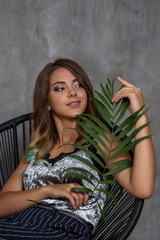 Fototapeta na wymiar Closeup woman portrait. Young contented fashionable girl posing in sitting in a chair. Fashion. Palm leaf on background