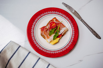 slice of bread with smoked ham, cheese and tomatoes on red plate