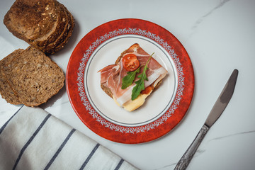 slice of bread with smoked ham, cheese and tomatoes on red plate