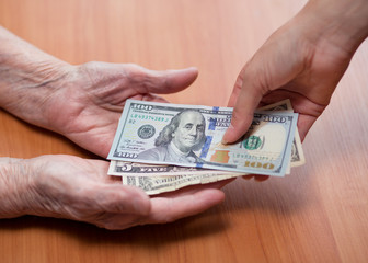 Paper notes in the hands of an old woman. Handing over money. An elderly man takes money from the hands of a young girl. Financial assistance concept. Senior citizen and money.